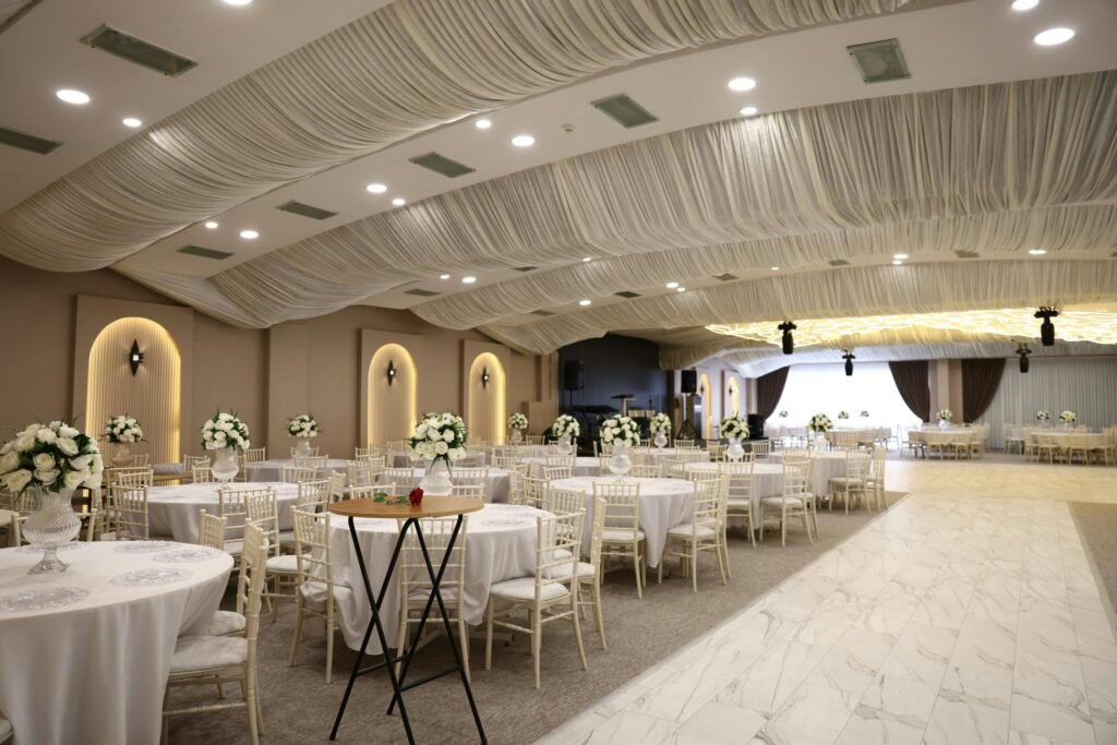Services Spacious and elegantly decorated ballroom for a wedding reception with floral arrangements and draped ceiling.
